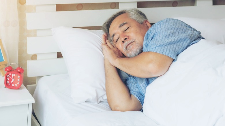 Older man asleep in bed next to red alarm clock
