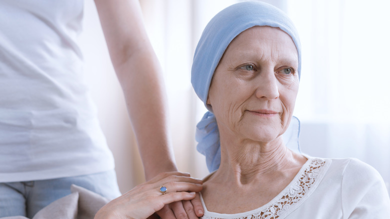 Hand supportively placed on shoulder of woman wearing head scarf: cancer patient concept