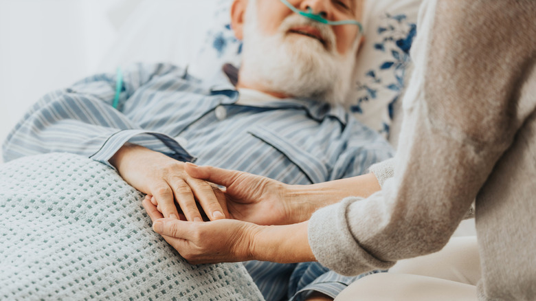 terminally ill man holding hand of a caregiver