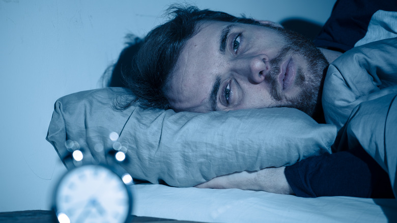 Man in bed gazing at alarm clock