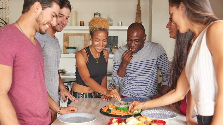 young adult friends eating buffet foods on table at home