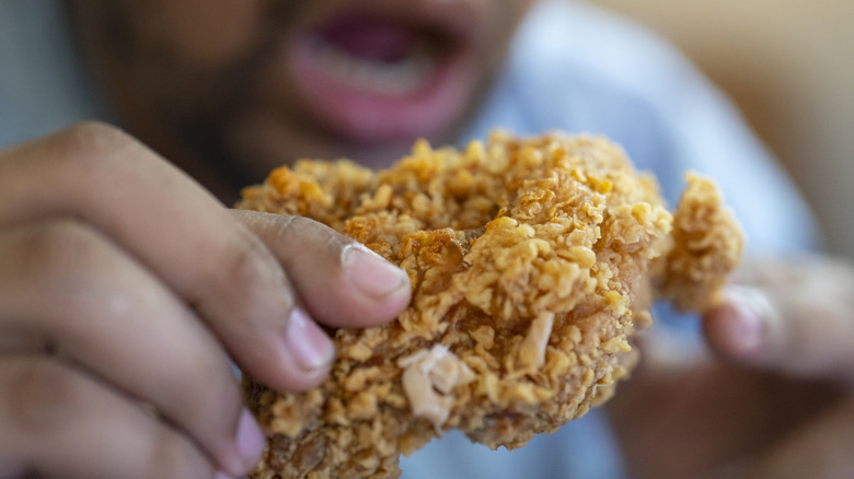 man about to bite into a fried chicken piece