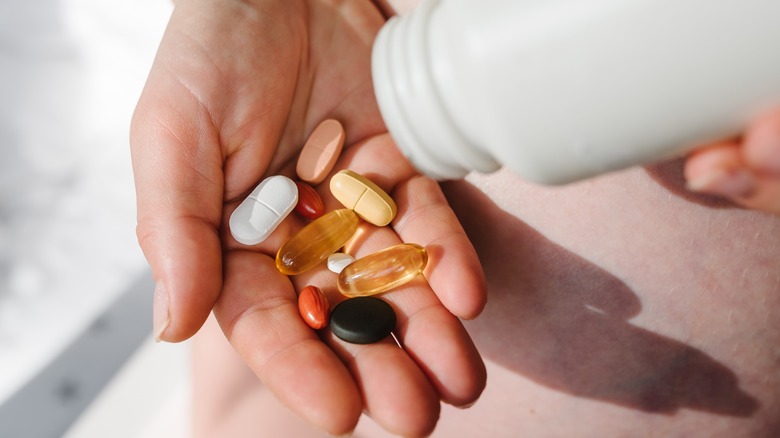 hand holding multiple supplement pills and capsules