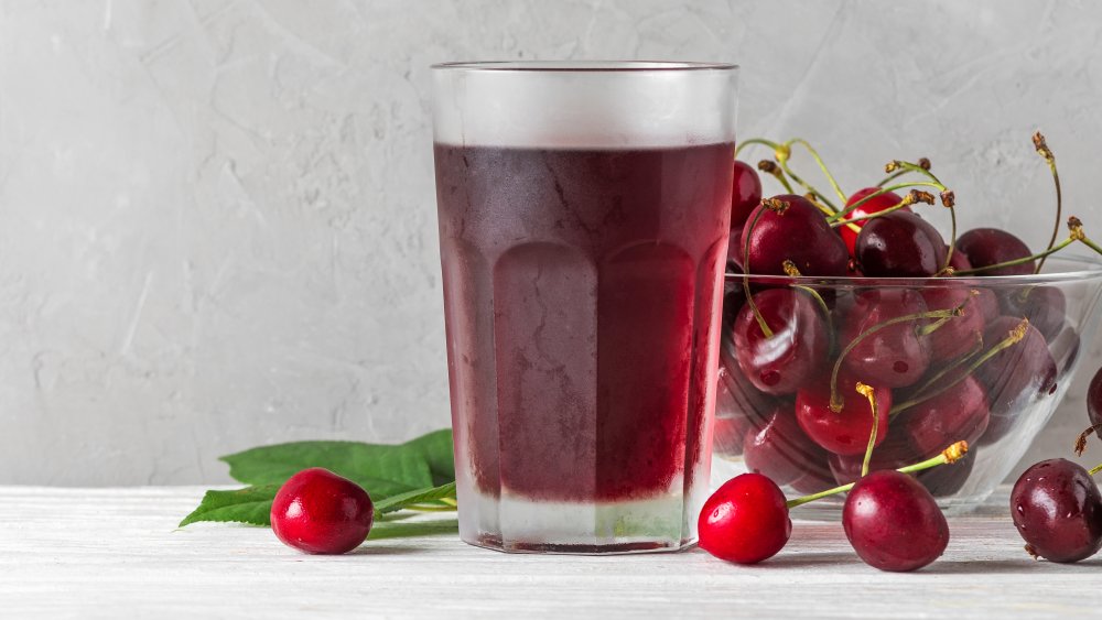 A glass of cherry juice with a bowl of cherries on the side 