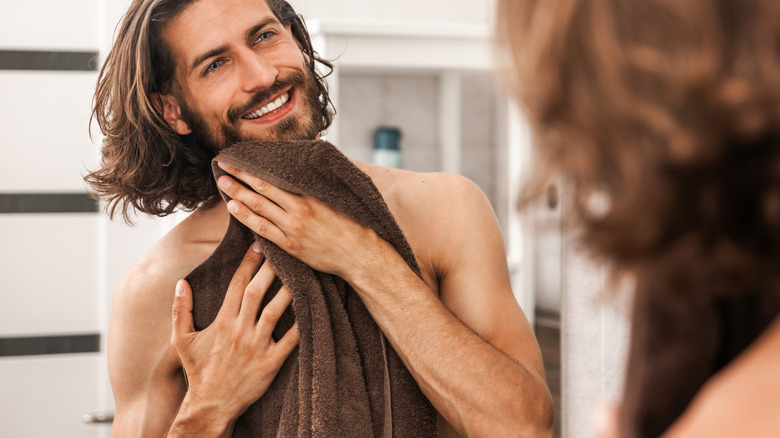 Bearded man with towel at face looking in mirror