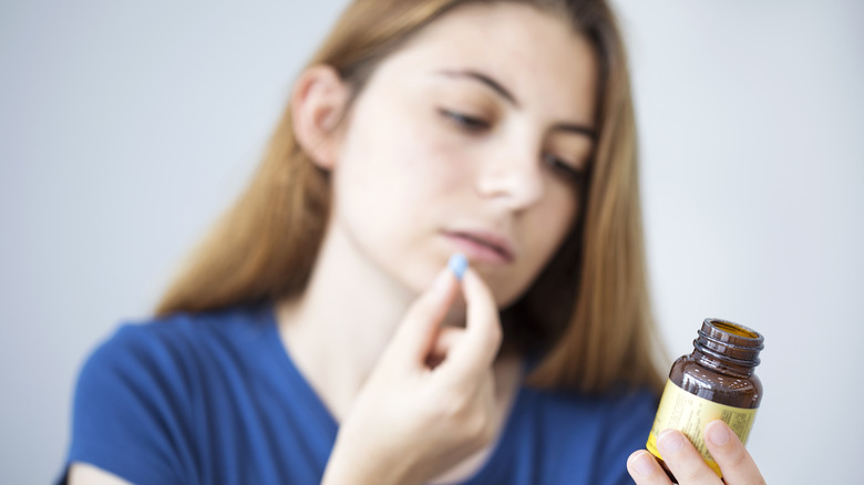 woman taking pill while reading medicine bottle