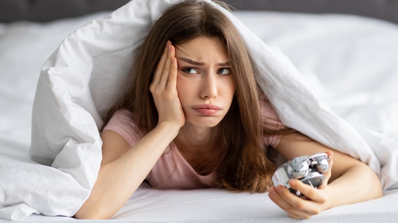 A woman in bed, with alarm clock