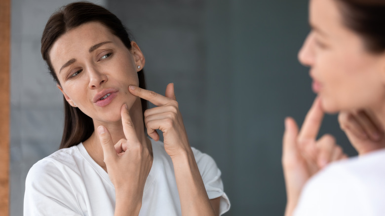 Woman examines face in the mirror