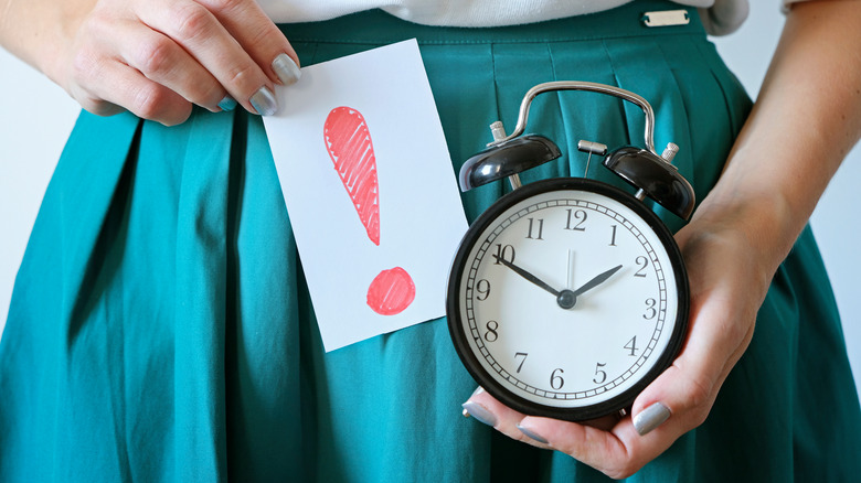 Woman holding up a red exclamation point and alarm clock 