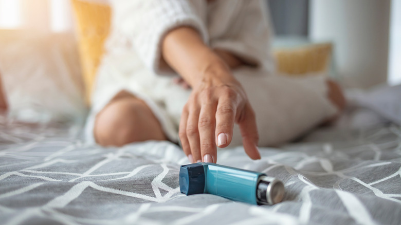 Hand reaching for inhaler on bed