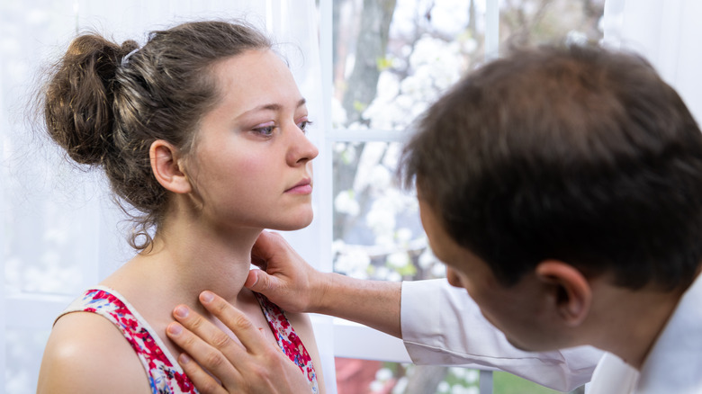 doctor palpating woman's neck for checkup