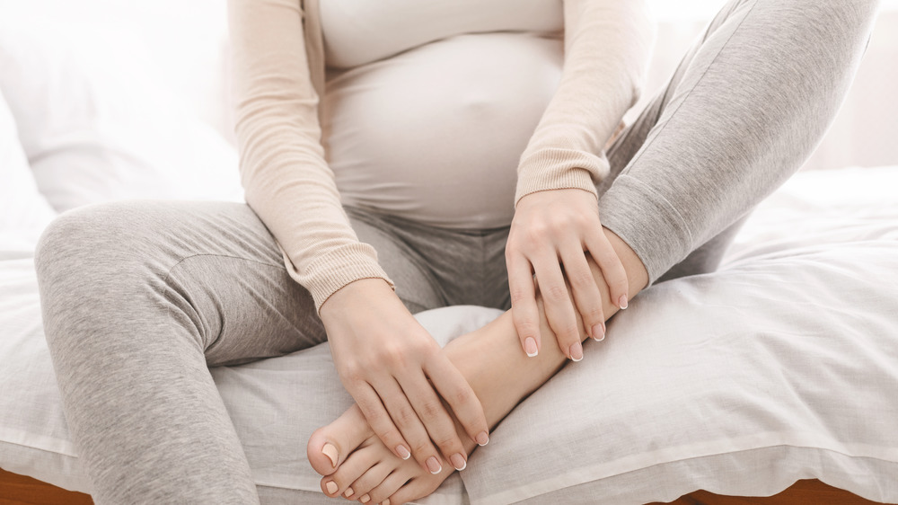 Pregnant woman holding swollen foot
