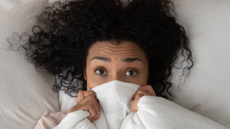 black woman with curly hair in bed embarassed