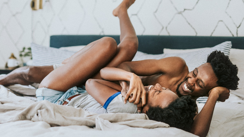 happy black couple laying in bed playing 