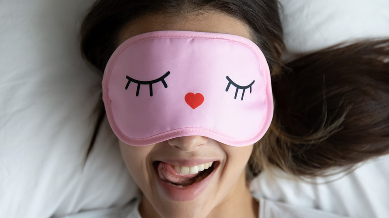 Woman laying in bed happy with eye mask smiling