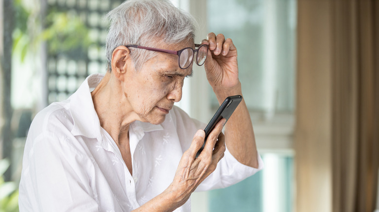 Senior citizen lifting up glasses and squinting while trying to see something on her cellphone