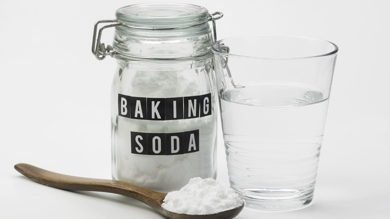 Baking soda in a jar, on a spoon, alongside glass of water