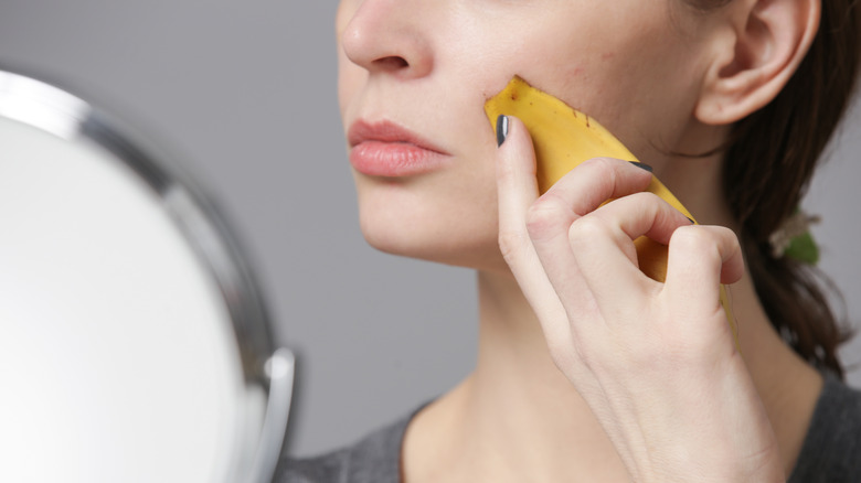 A woman rubs a banana peel on her face