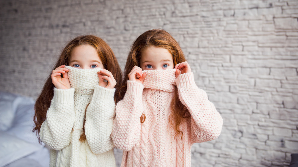 Two redheaded twins pulling turtlenecks over their faces