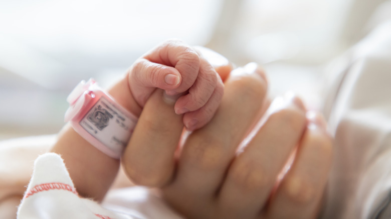 Newborn baby holding woman's hand