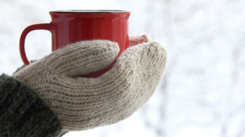 person wearing mittens and holding a mug
