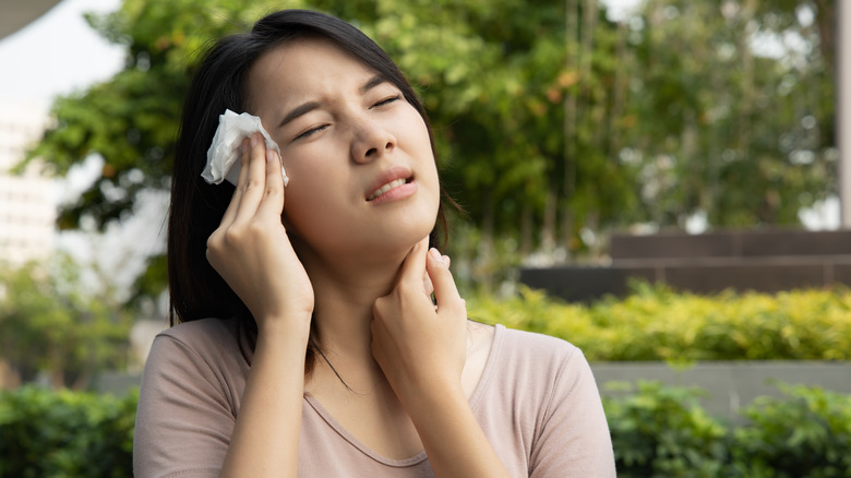 woman outside blotting her face in discomfort