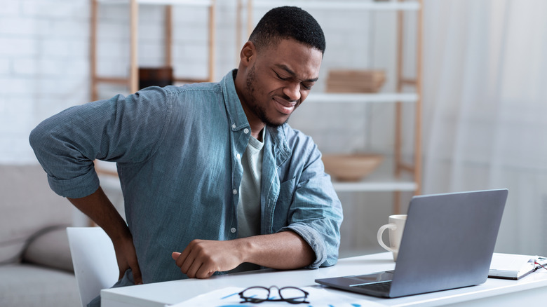 man with lower back pain grimacing at desk 