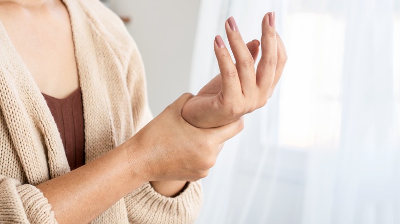 person in sweater holding their left hand 