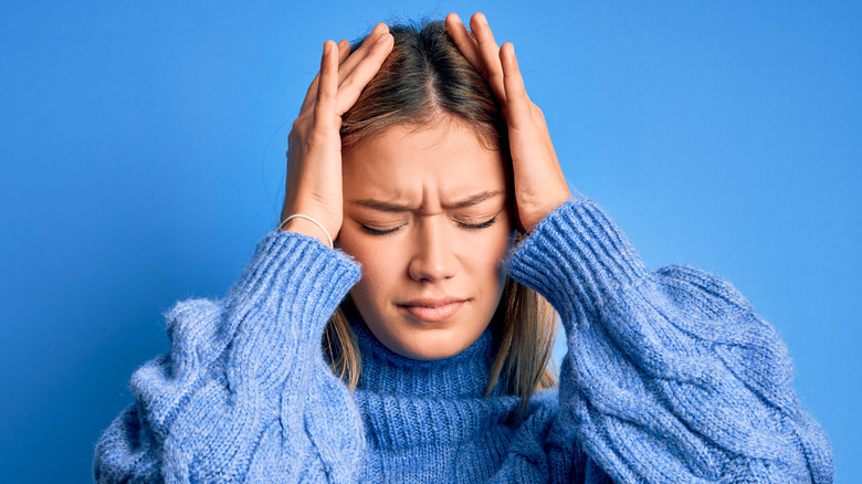 woman in sweater holding her head in pain