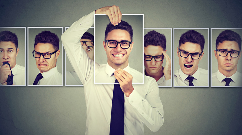 Man in glasses and a tie holding up a photo of himself smiling in front of his face and in the background are other photos of him each expressing a different mood