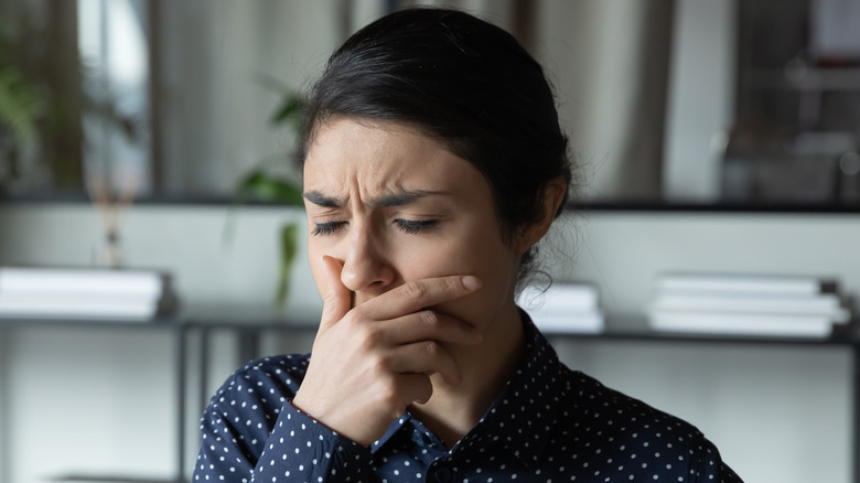 Woman in a polka dotted navy blue shirt holding her hand over her mouth in distress