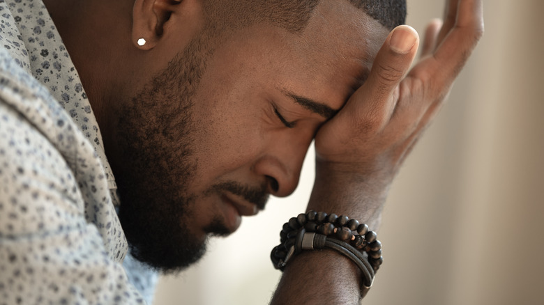 Close up of a man with his eyes closed holding his head in exhaustion