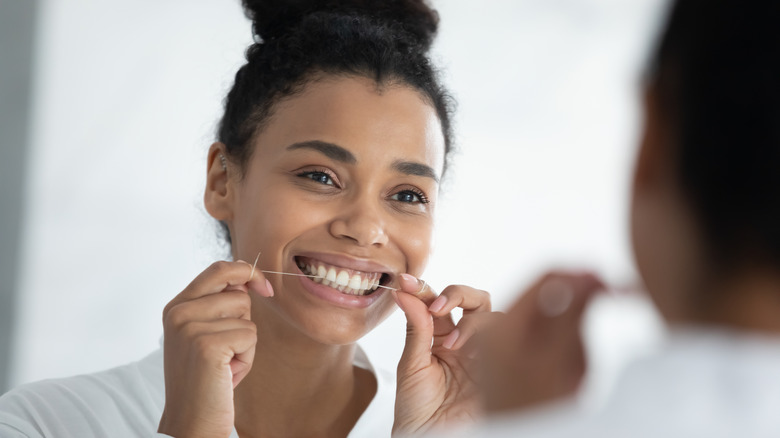 Woman in a white bathrobe smiling while flossing her teeth