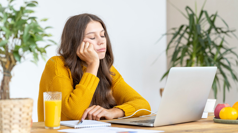 Woman in a yellow sweater dozing off in front of her laptop