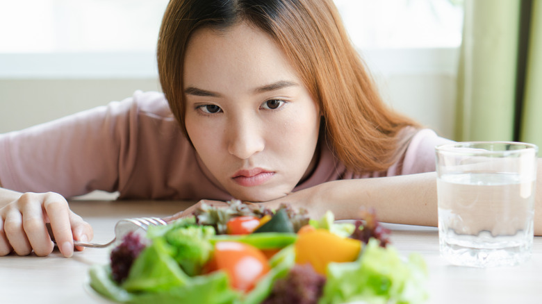 Woman looking unhappily at a plate of vegetables  