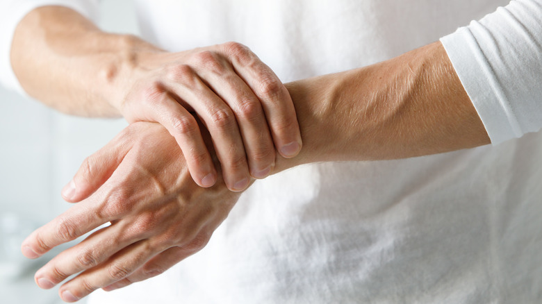 Close up of a person in a white shirt holding their wrist to demonstrate arthritis