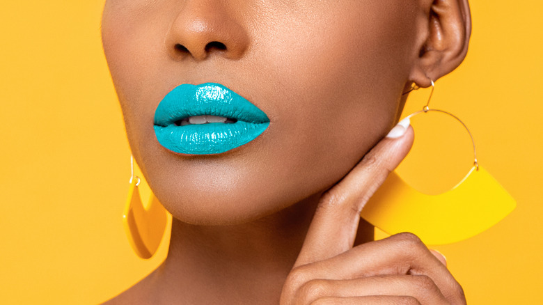 Close up of a woman wearing blue lipstick and large, yellowing earrings