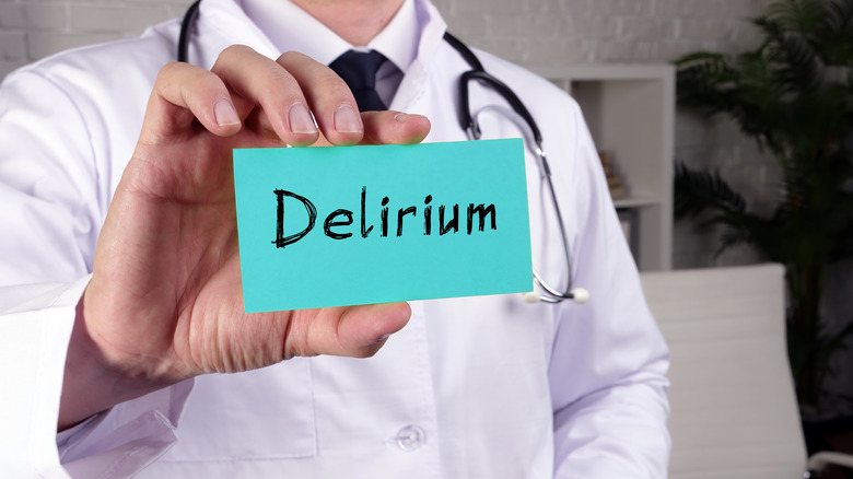 Close up of a doctor in a white coat holding up a card that reads "Delirium"