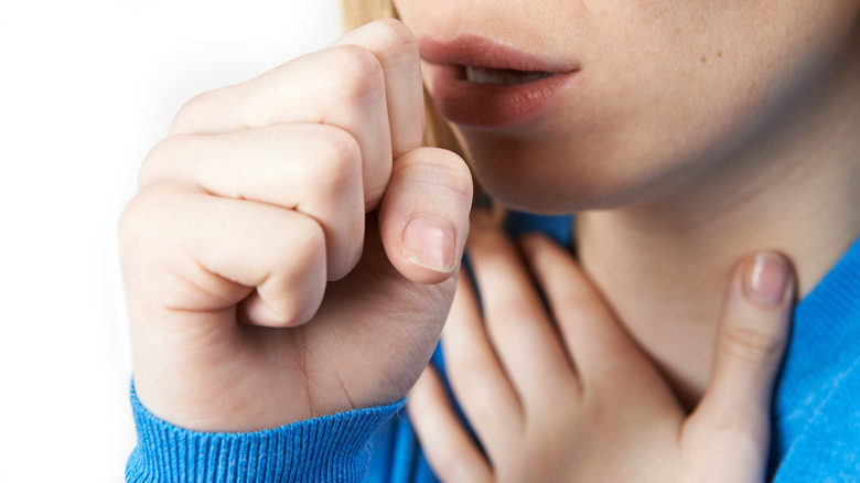 Close up of a woman in a blue shirt coughing into her fist