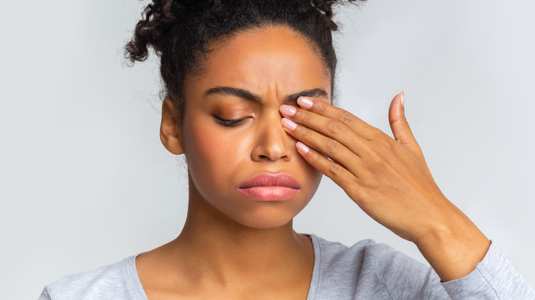 Woman in a gray shirt holding her hand over her eye while looking down