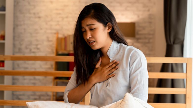 Woman sitting up in bed holding her chest because she's having difficulty breathing