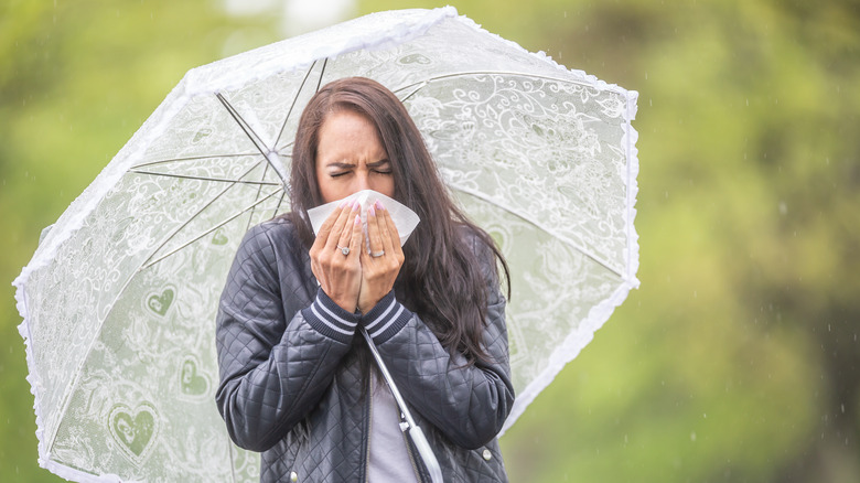 Woman with a white umbrella holding a tissue to her face