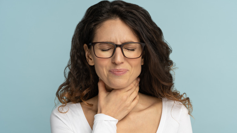 Woman with sore throat wincing and holding throat in pain