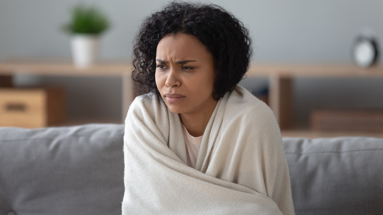 A woman looking uncomfortable as she holds a blanket around herself
