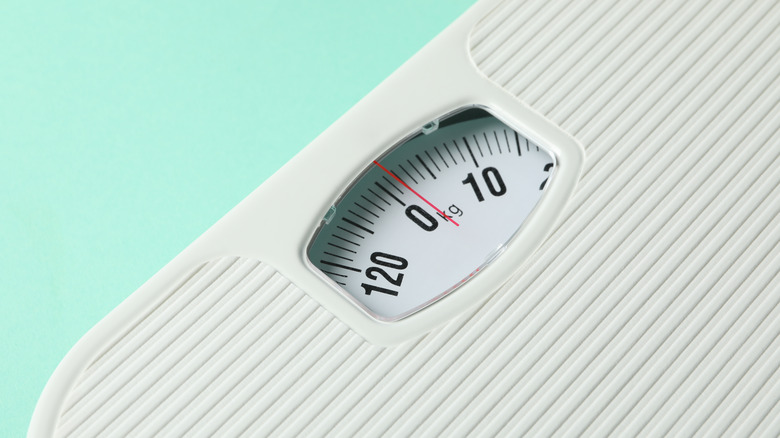 A close of a bathroom scale at zero against a light blue background