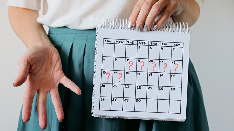 Close up of a woman with sliver nails holding up a calendar with red question marks on it