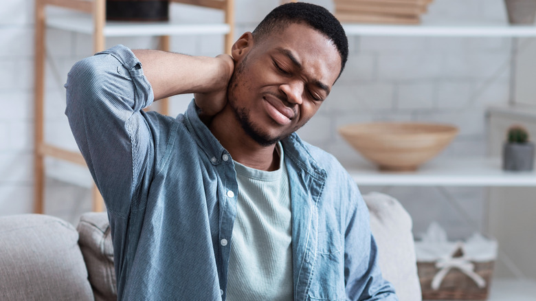 Man holding his neck in discomfort while sitting on a couch