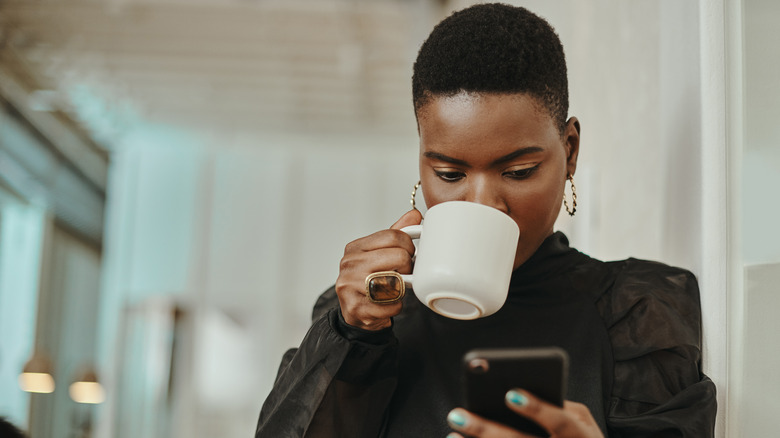 Woman drinking coffee, looking at phone