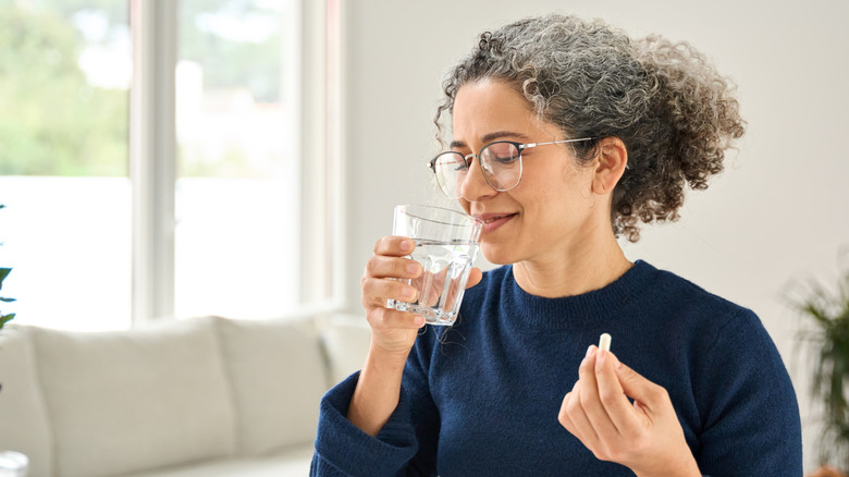 A middle age woman taking a supplement with a glass of water