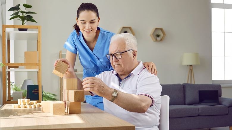 A health aide assisting an older man assembling wood blocks